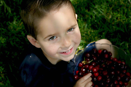 a young boy sits in the grass with a big bowl of cherries の写真素材