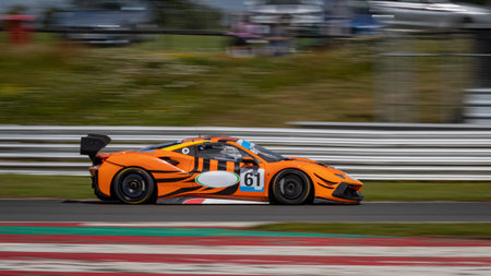 A panning shot of an orange and black racing car as it circuits a track.