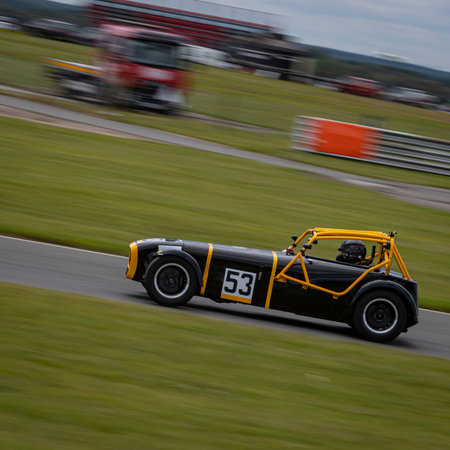 A panning shot of a black and yellow racing car as it circuits a track.