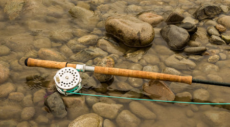 Spey fly fishing salmon rod and reel resting on wet rocks beside a river.