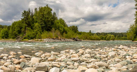 A boulder strewn, fast flowing Kitimat river, beside a forest, on a cloudy day, in British Columbia.の写真素材