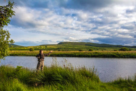 A fisherman fly fishing in the evening sun on the Blackwater of Dee, Galloway, Scotlandの写真素材