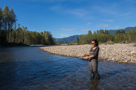 An asian women in waders, enjoying fishing the Kitimat River, Skeena Region, in British Columbia,...