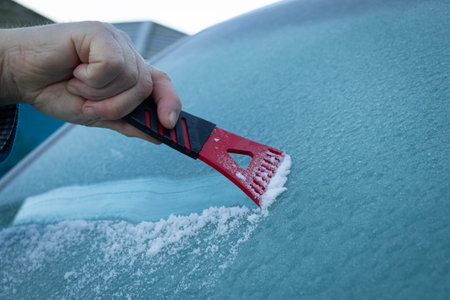 A man scraping ice off a frozen wind shield or screen of a vehicle on a cold winters morning