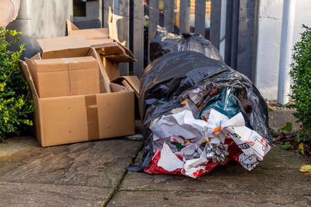 Christmas household waste consisting of boxes and wrapping paper, beside a bin or trash can in a gardenの写真素材