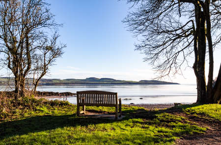 Wooden bench overlooking the sea at Dhoon Bay on a sunny winter morning, Kirkcudbright, Scotlandの写真素材