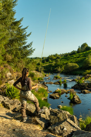 An asian female fly fisher women wearing waders and holding a rod, looking where to fish on a riverの写真素材