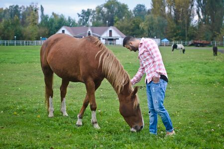 Young handsome guy Cowboy. man is a farmer in his ranch where there are many horses. Rural landscapes, countryside. Stock photosの写真素材