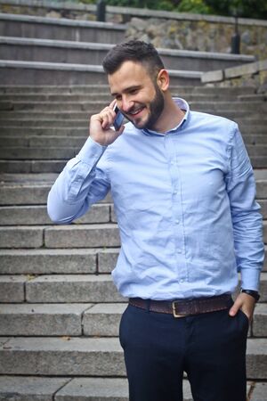 Portrait of a bearded man near the big steps of an old European castle. Businessman talking on the phone. Fashionable guy with stylish clothes.の写真素材