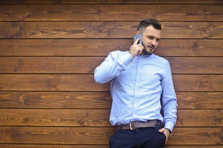 Portrait of a handsome man in a shirt on a wooden wall background. Businessman, boss in stylish clothes. Sexy guy talking on the phone. Stock Photo designの写真素材