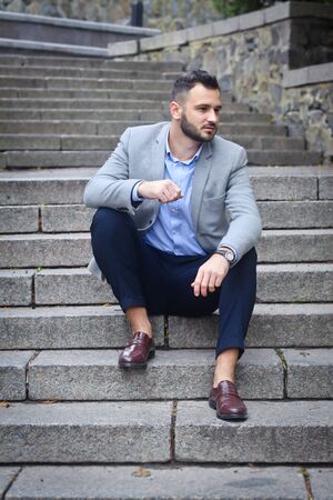 Portrait of a bearded man near the big steps of an old European castle. Businessman thinking over a future project. Fashionable guy with stylish clothes.の写真素材