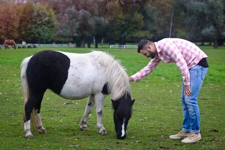 Young handsome guy Cowboy. man is a farmer in his ranch where there are many horses. Rural landscapes, countryside. Stock photosの写真素材