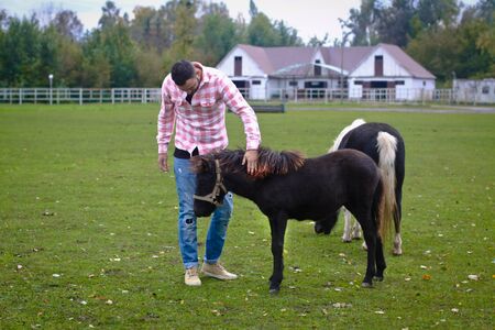 Young handsome guy Cowboy. man is a farmer in his ranch where there are many horses. Rural landscapes, countryside. Stock photosの写真素材
