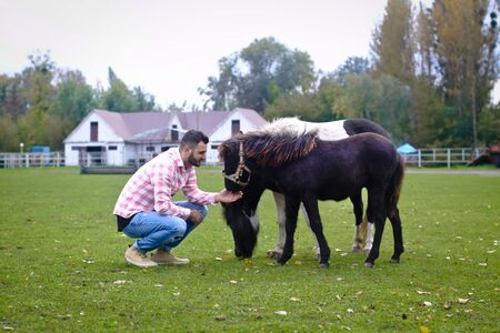 Young handsome guy Cowboy. man is a farmer in his ranch where there are many horses. Rural landscapes, countryside. Stock photosの写真素材