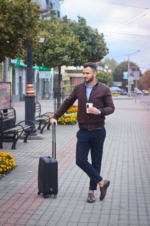 Handsome man with a suitcase for tourism. Exit the house for travel. Fashionably dressed guy and coffee. Stock Photo.の写真素材