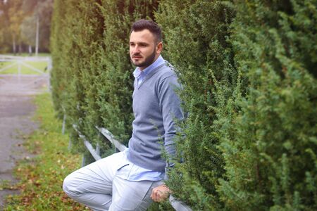 Young guy on the background of European, American city. man in the background of trees and fields and fence. The owner of a beautiful land for businessの写真素材