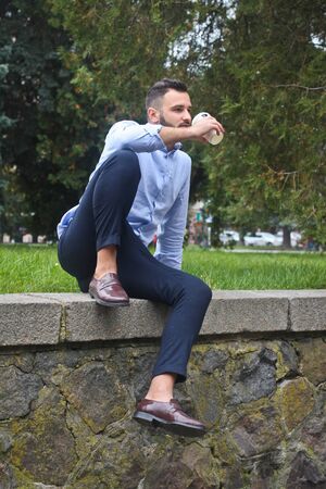 Portrait of a guy in a shirt sitting in a park in a European city. A man in the background of trees and buildings. Stock photosの写真素材