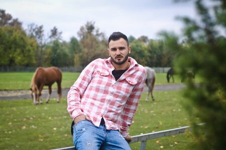 Young handsome guy Cowboy. A man is a farmer at his ranch near the fence. Rural landscapes, countryside. Trees, field, farm. Stock photosの写真素材