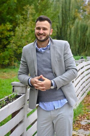 Portrait of a sexy man dressed in a suit. Fashionable guy in the autumn nature near a white wooden fence. Businessman relaxes. Skok photo for designの写真素材