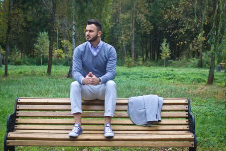Young sexy guy sitting on a bench in an autumnal, summer park. A man contemplating new ideas while walking. European countryside. Stock Photoの写真素材