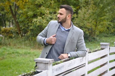 Portrait of a sexy man dressed in a suit. Fashionable guy in the autumn nature near a white wooden fence. Businessman relaxes. Skok photo for designの写真素材