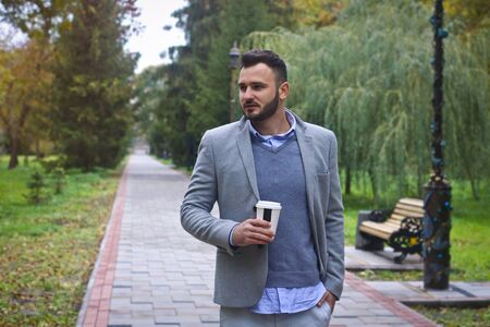Young sexy guy strolling through the autumn, summer park. man drinking coffee, tea in the nature. European countryside. Stock Photo for designの写真素材