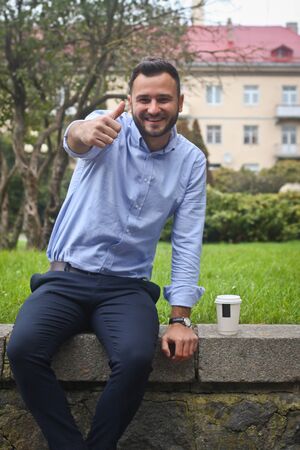 Portrait of a guy in a shirt sitting in a park in a European city. A man in the background of trees and buildings. Stock photosの写真素材
