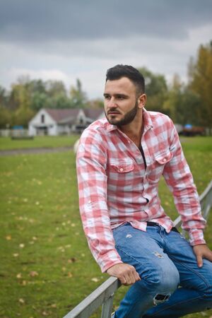 Young handsome guy Cowboy. A man is a farmer at his ranch near the fence. Rural landscapes, countryside. Trees, field, farm. Stock photosの写真素材
