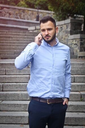 Portrait of a bearded man near the big steps of an old European castle. Businessman talking on the phone. Fashionable guy with stylish clothes.の写真素材