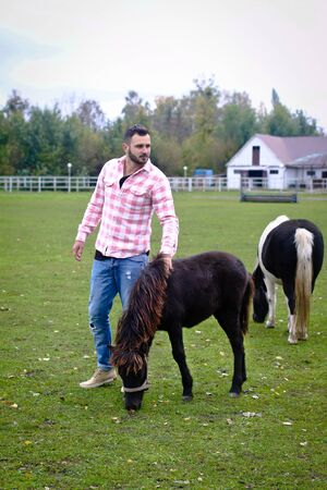 Young handsome guy Cowboy. man is a farmer in his ranch where there are many horses. Rural landscapes, countryside. Stock photosの写真素材