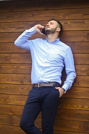 Portrait of a handsome  in a shirt on a wooden wall background. Businessman, boss in stylish clothes. Sexy guy talking on the phone.   designの写真素材