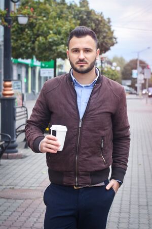 Man in a jacket and suit on a European street with coffee in his hands. Business guy fashion clothes. Autumn landscape, portrait. stock photoの写真素材
