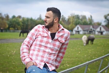 Young handsome guy Cowboy. A man is a farmer at his ranch near the fence. Rural landscapes, countryside. Trees, field, farm. Stock photosの写真素材