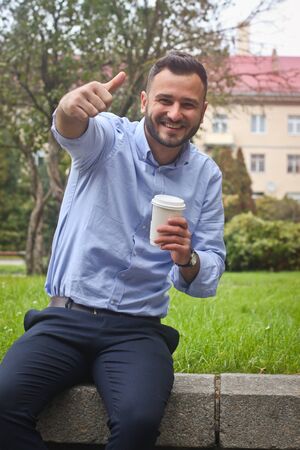 Portrait of a guy in a shirt sitting in a park in a European city. A man in the background of trees and buildings. Stock photosの写真素材