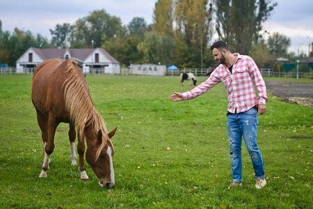 Young handsome guy Cowboy. man is a farmer in his ranch where there are many horses. Rural landscapes, countryside. Stock photosの写真素材