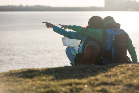 Tourist couple sitting on grass and looking at waterの写真素材