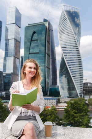 Young pretty woman sitting against office buildings with green notebook or diary.の写真素材
