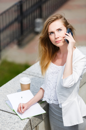 Young businesswoman talking on cellphone while walking outdoor.の写真素材