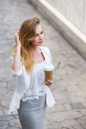 Young stylish woman drinking coffee to go in a city streetの写真素材