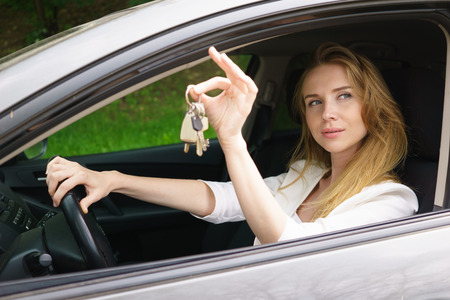 Young woman showing key sitting in carの写真素材