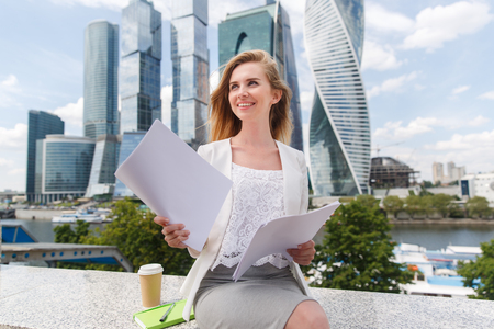 young smiling businesswoman with heap of papers sitting on city benchの写真素材