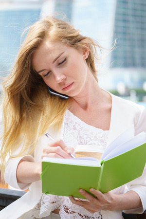 Businesswoman taking notes white talking by phone and drinking coffeeの写真素材