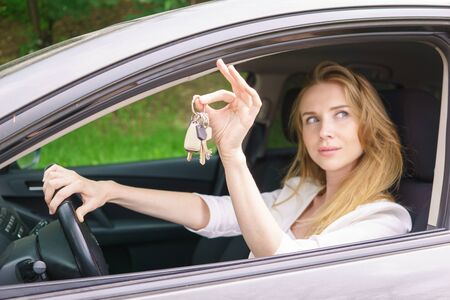 Young woman showing key sitting in carの写真素材