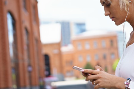 Beautiful young woman with blonde hair messaging on the smart-phone at the city streetの写真素材