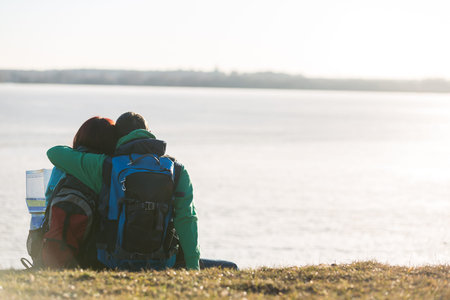 Tourist couple sitting on grass and looking at water
