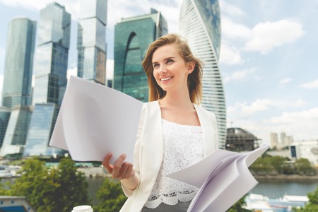 young smiling businesswoman with heap of papers sitting on city benchの写真素材