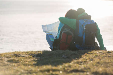 Tourist couple sitting on grass and looking at waterの写真素材