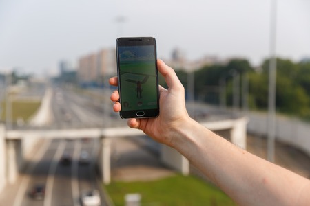 Man held phone in one hand showing its screen with Pokemon Go application on city backgroud. Moscow, Russia.のeditorial素材