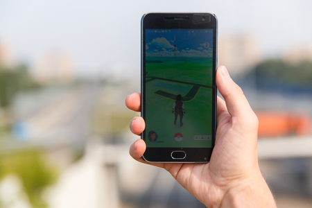 Man held phone in one hand showing its screen with Pokemon Go application on city backgroud. Moscow, Russia.のeditorial素材
