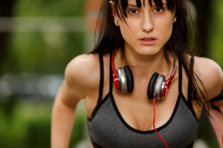 Closeup outdoors portrait of young athletic dark-haired woman with headphones